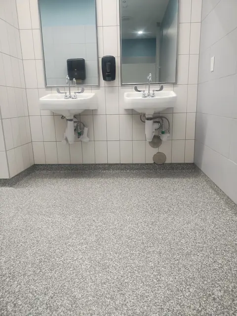 Multi-color quartz floor and cove base in a tiled restroom